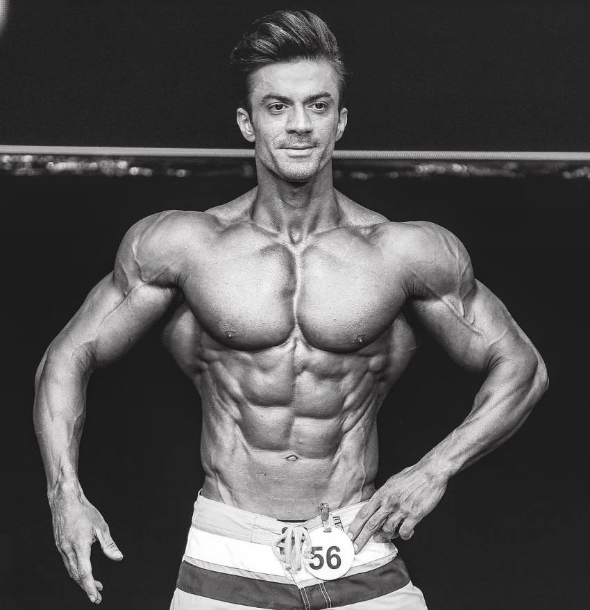 Black and white picture of Mohammad Kashanaki on the men's physique stage, looking ripped and muscular