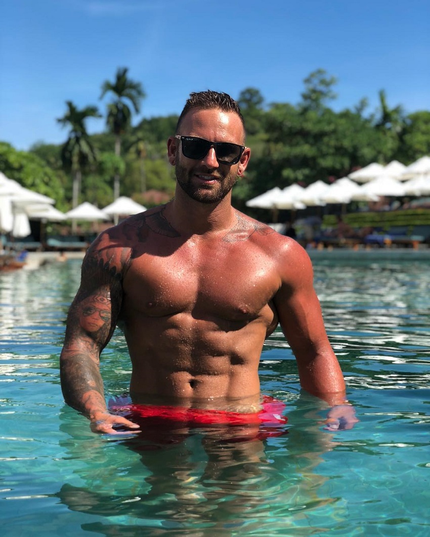 Joel Bushby standing half-way in the pool looking muscular and ripped